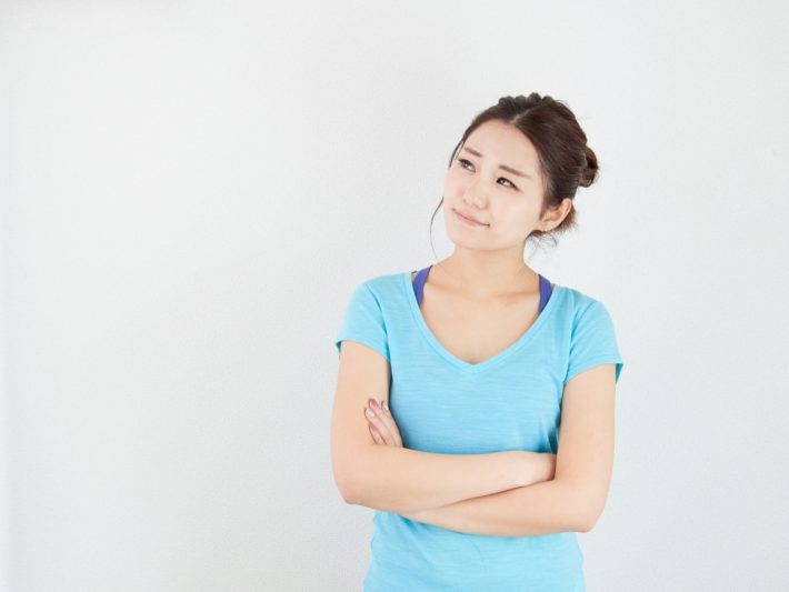 水色の服を着た女性が腕を組んで悩んでいる画像