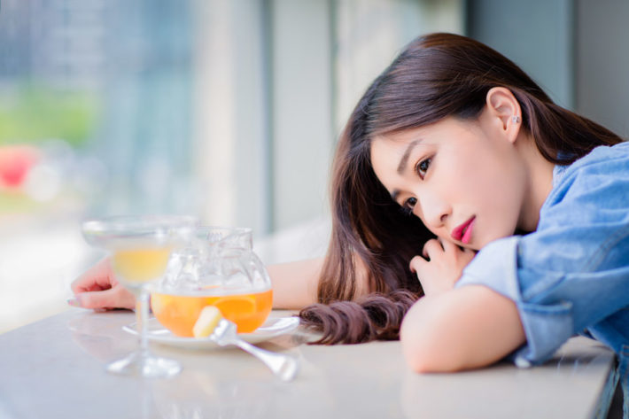 カフェのテーブルに顔を伏せて窓の外を眺める女性