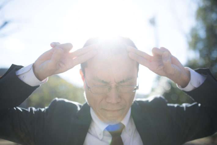 太陽を背に頭に指を当て太陽拳のポーズをとる男性
