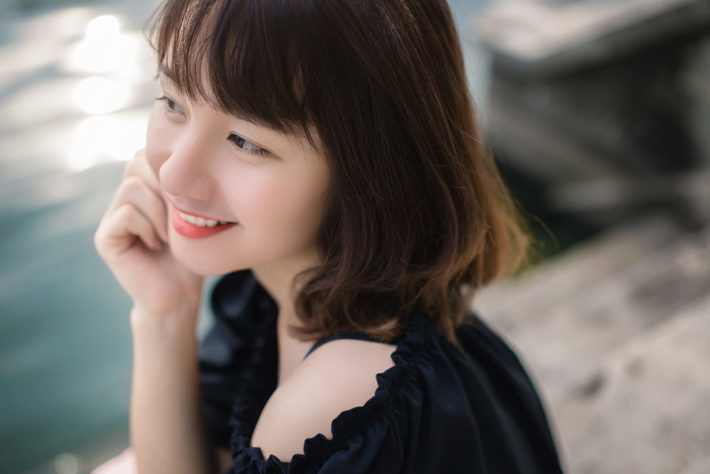 水辺で頬に手をつき笑っている女性