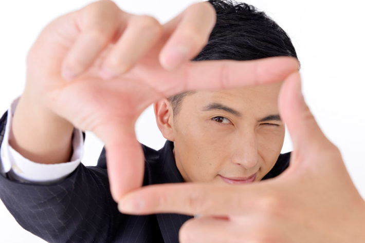 手でカメラのフレームを作り覗き込んでいる男性