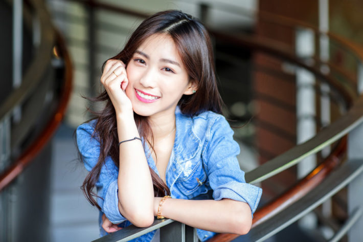 手すりに寄りかかり微笑んでいるロングヘアの女性