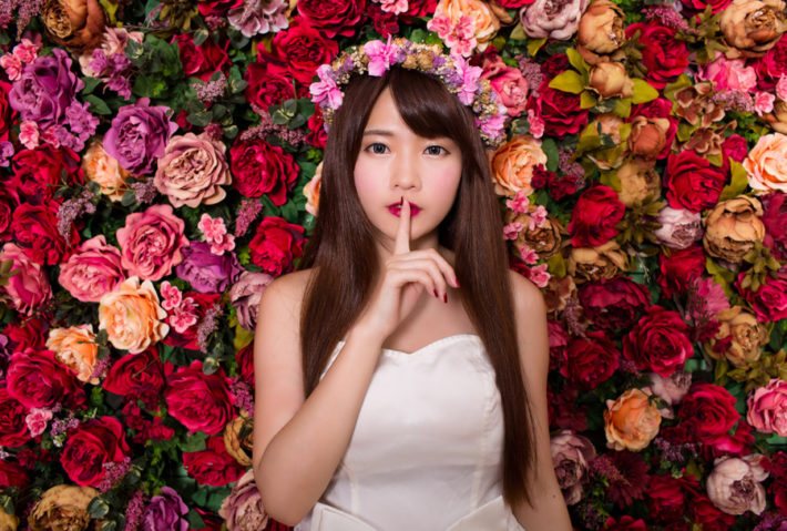 花かんむりをして口元に人差し指をあてている女性