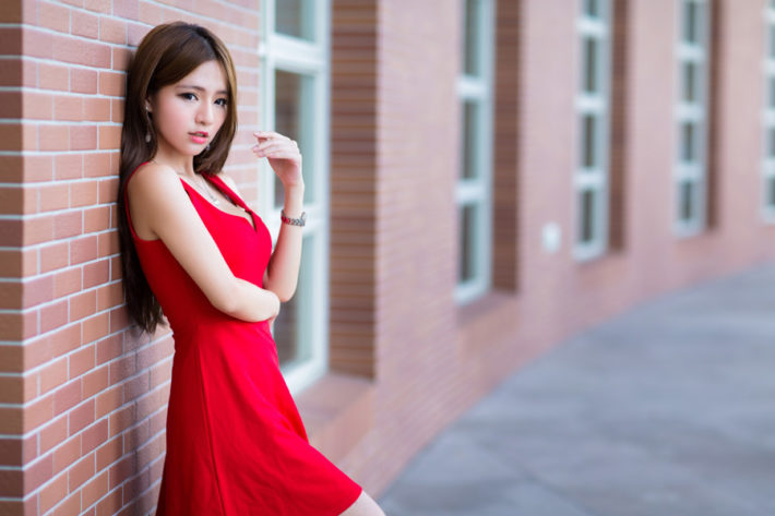 レンガ壁にもたれているワンピース姿の女性