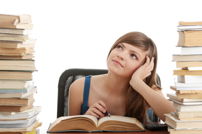 山積みの本に囲まれて考え事をしている女性