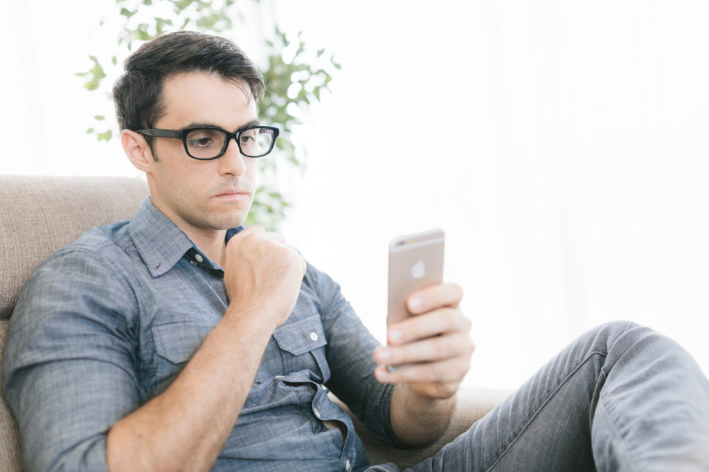 ソファーでスマホを使う眼鏡の男性