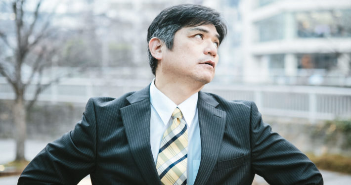 呆れた顔で空を見上げているスーツ姿の中年男性
