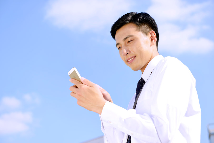 青空の下でスマホを使っている笑顔の男性