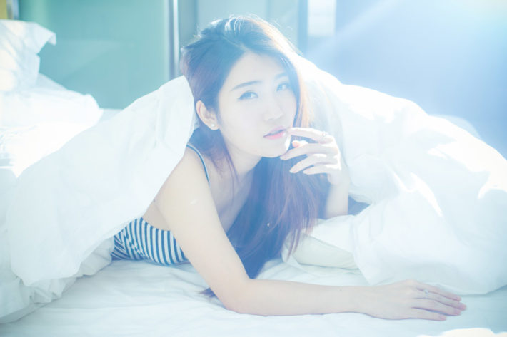 ベッドでシーツを羽織りうつ伏せになっている女性