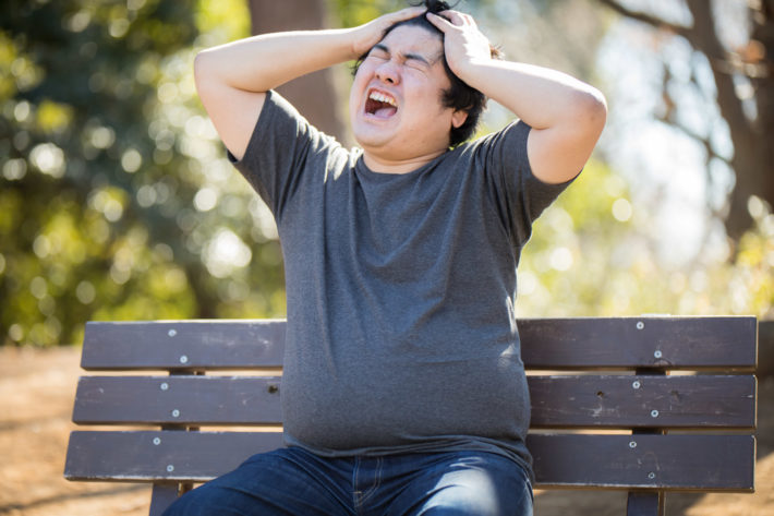 公園のベンチで頭を抱えて悩んでいる男性
