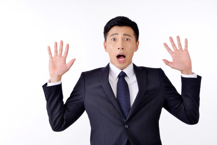 手を広げて驚くスーツ姿の男性