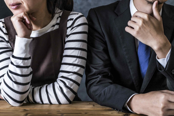 机に肘をつき、考え事をしている男女