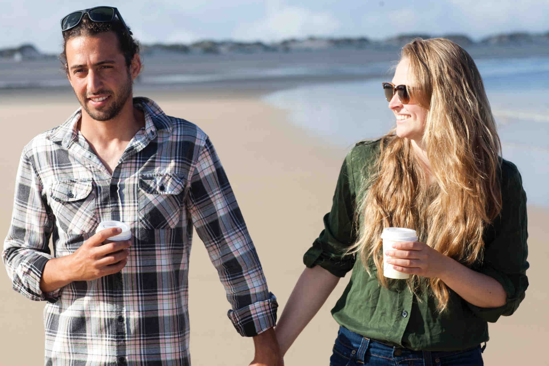 海辺を手をつないで歩くカップル