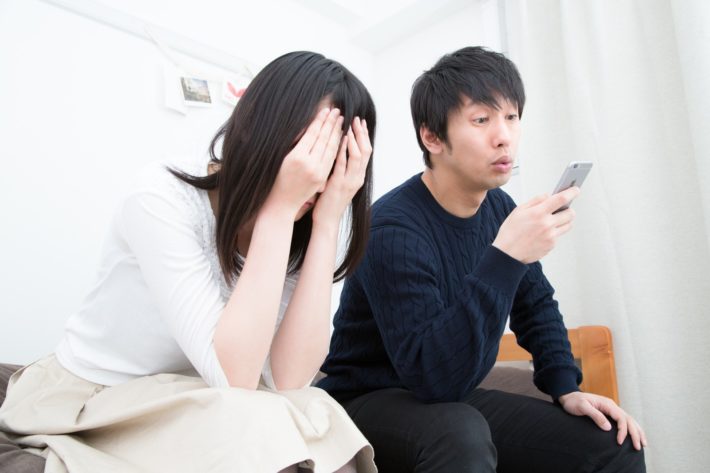 泣いている女性の隣でスマホをいじる男性