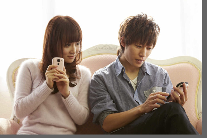 ソファーに座り携帯で遊ぶカップル