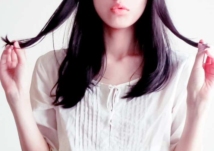 髪の毛の先を指で持つ女性