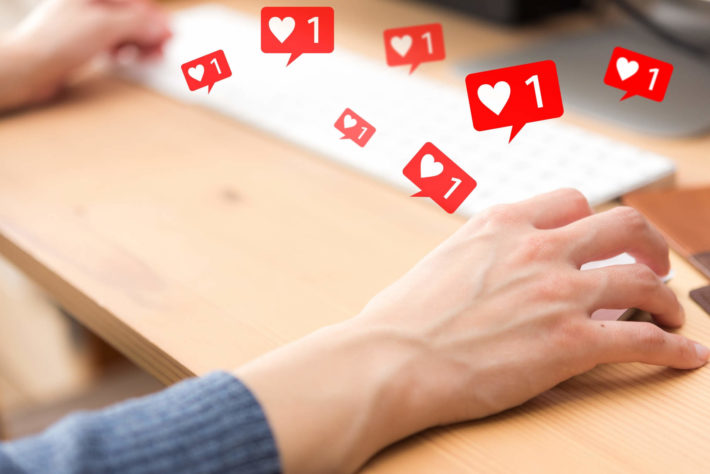 PCを操作している男性の手元と宙に浮かぶ無数のいいね