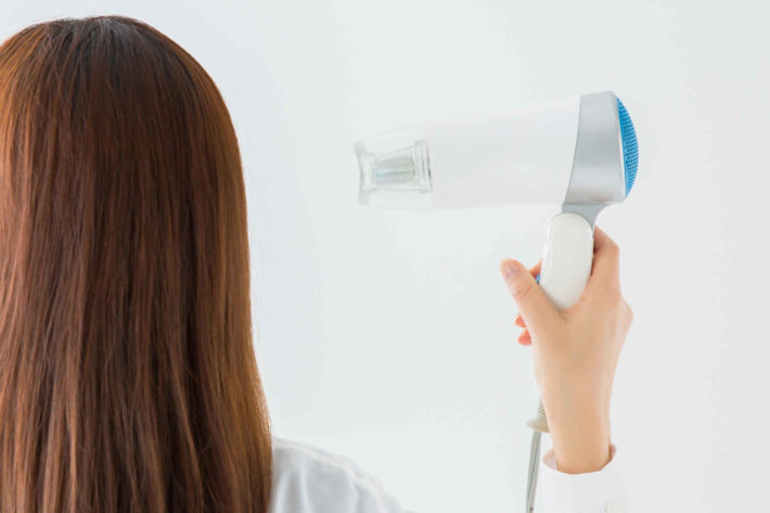 ヘアドライヤーで髪の毛を乾かしている女性