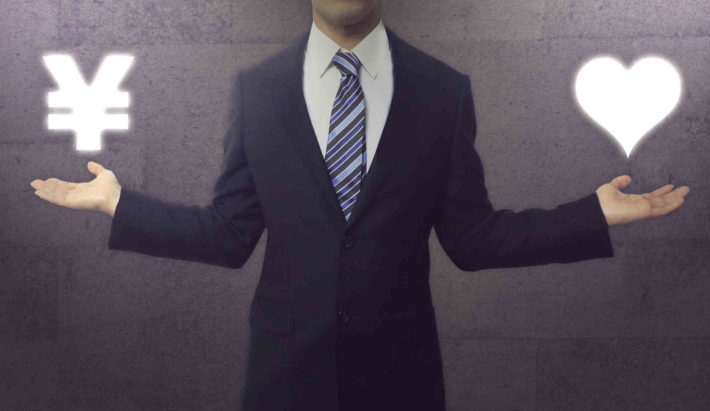 スーツの男性が両手にお金とハートを釣り合わせている画像