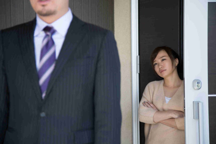 玄関先で夫を仕事に送り出している、しかめっ面の妻