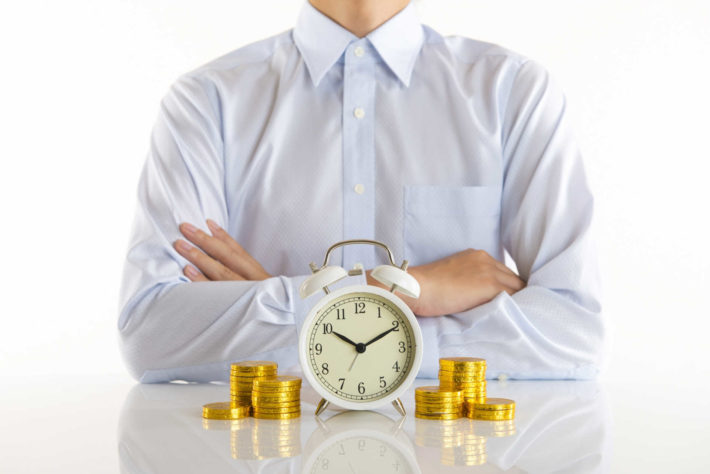 腕を組む男性とテーブルの上にある時計とコイン