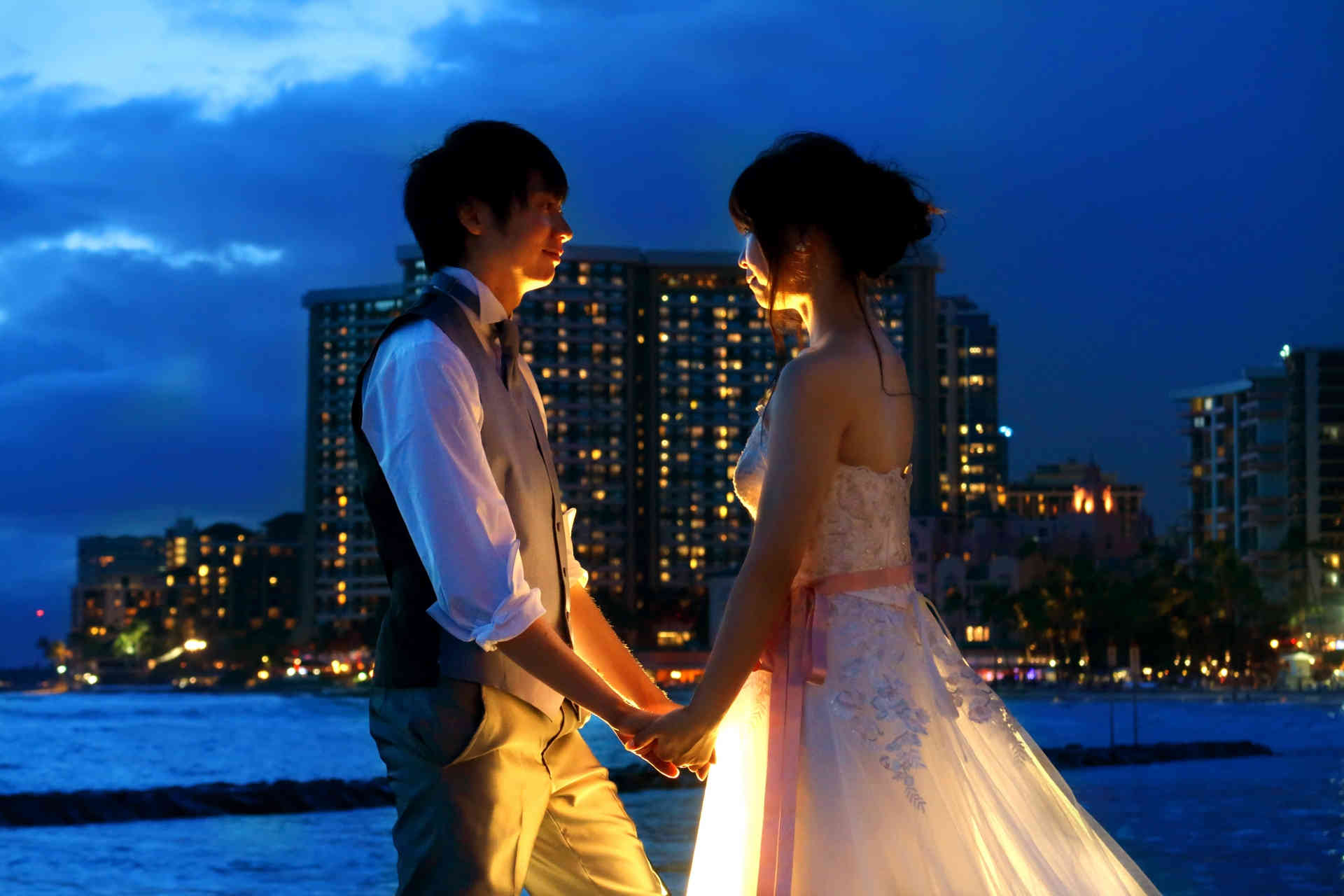 夜の海辺で結婚式を挙げ見つめ合っている男女