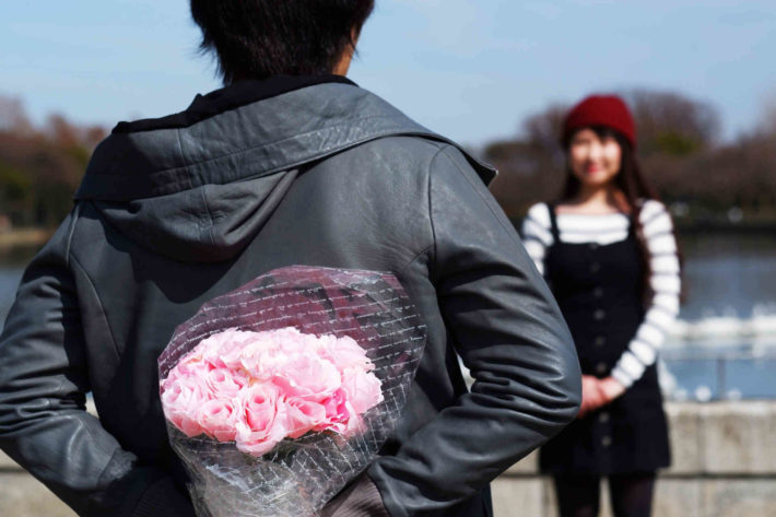 花束を背中に隠し、女性に渡そうとしている男性