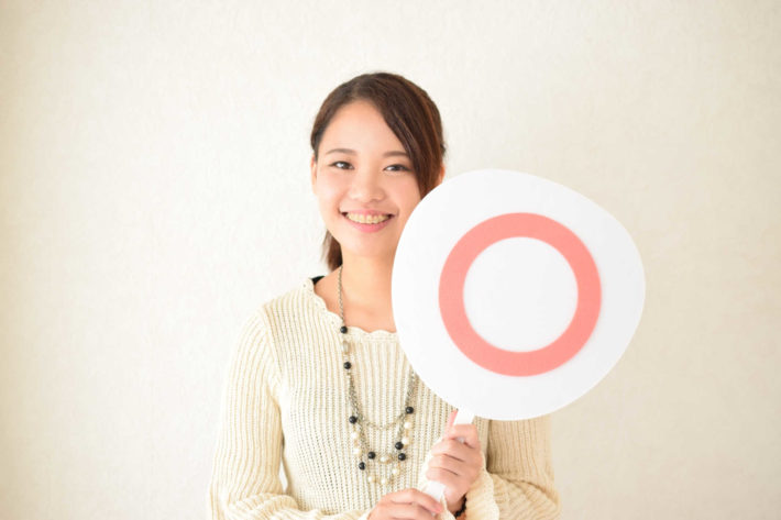 笑顔で「◯」が書かれた札を持つ女性