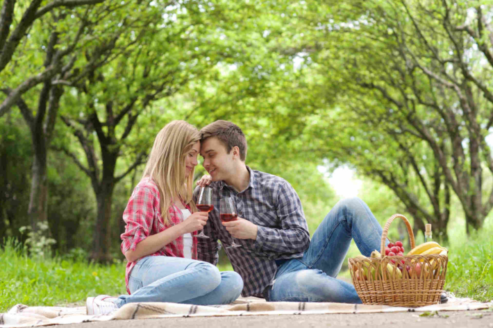 野外で広げたシートの上に座り、ワインを飲んでいる外国人の男女