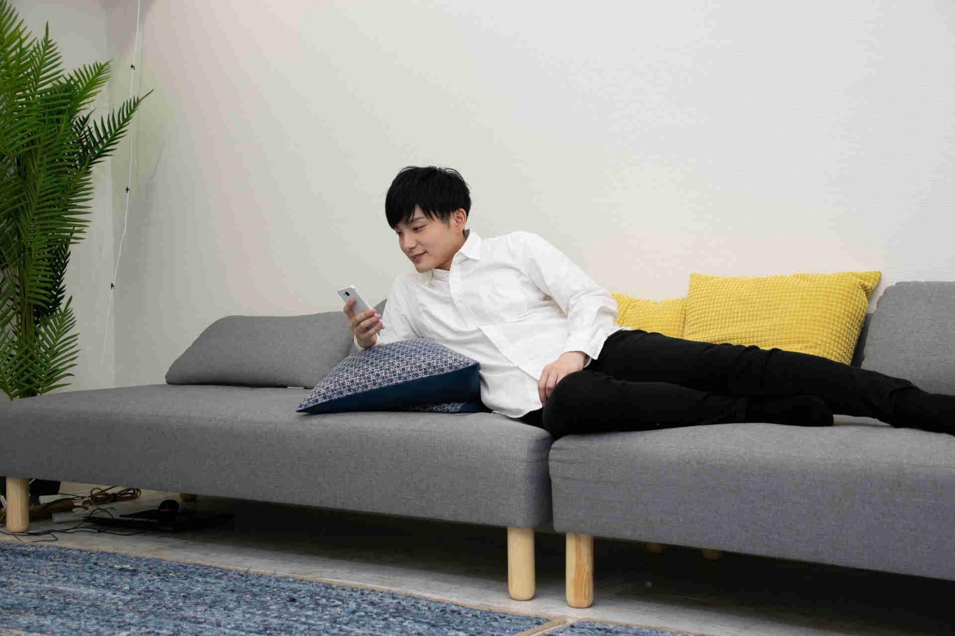 ソファーに寝そべりスマホを触っている男性