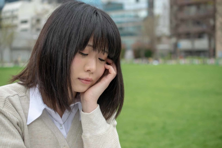 草むらで落ち込む様子の女子高生