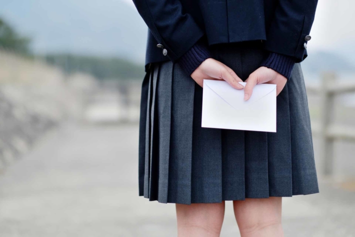後ろ手にラブレターを隠し持って誰かを待っている女子高生