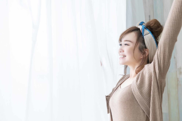 レースカーテン越しに外を見て伸びをする女性