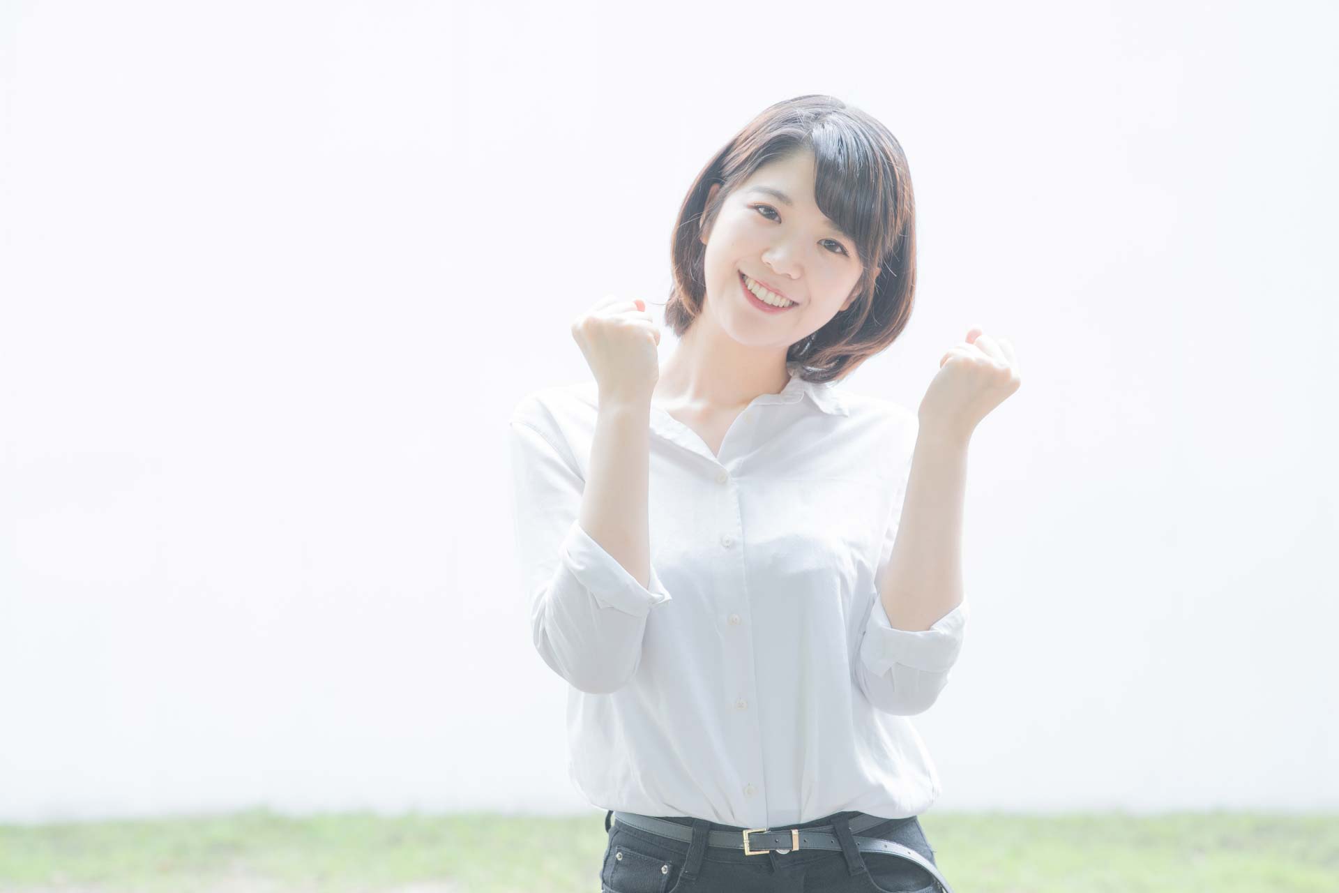 笑顔でガッツポーズしている白いブラウスを着た女性