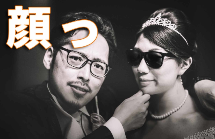 「顔っ」と書かれたテキストと結婚式を挙げているカップル