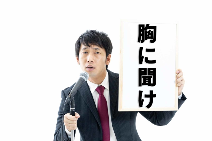 ホワイトボードを掲げて威圧する男性と「胸に聞け」の文字