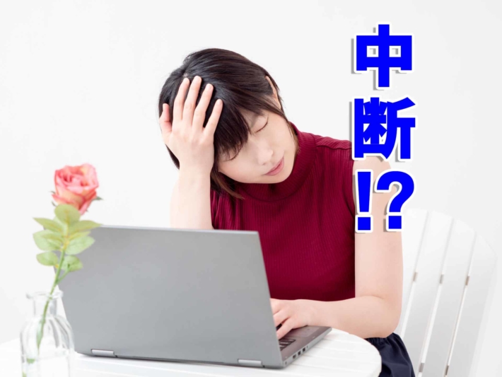 「中断!?」と書かれたテキストと、ノートPCの前で頭を抱える女性