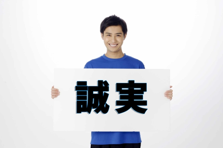 「誠実」と書かれたプラカードを持って笑う、さわやかな男性