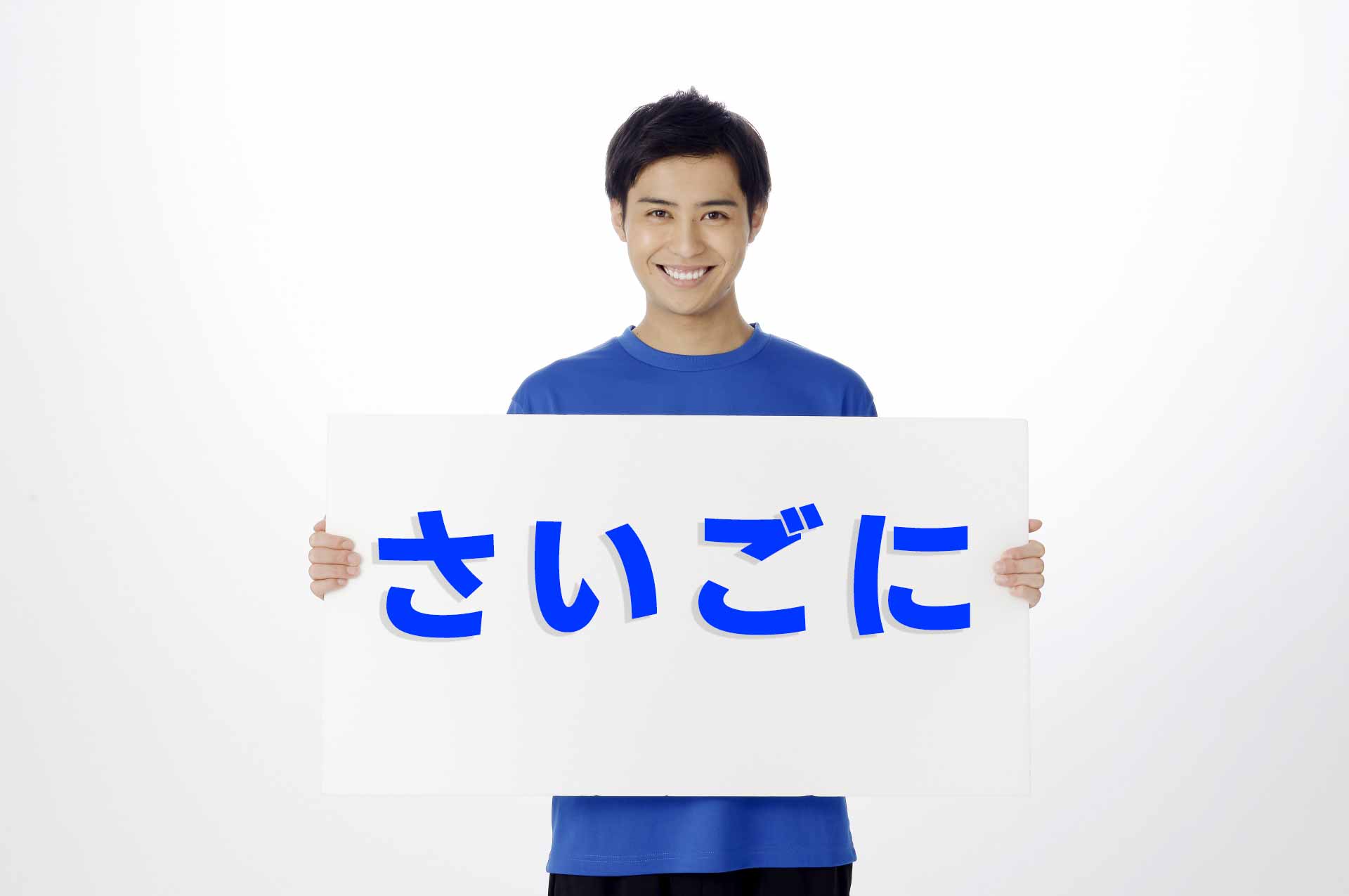 「さいごに」と書かれたプラカードを胸の前に持ち、笑顔で立っている男性