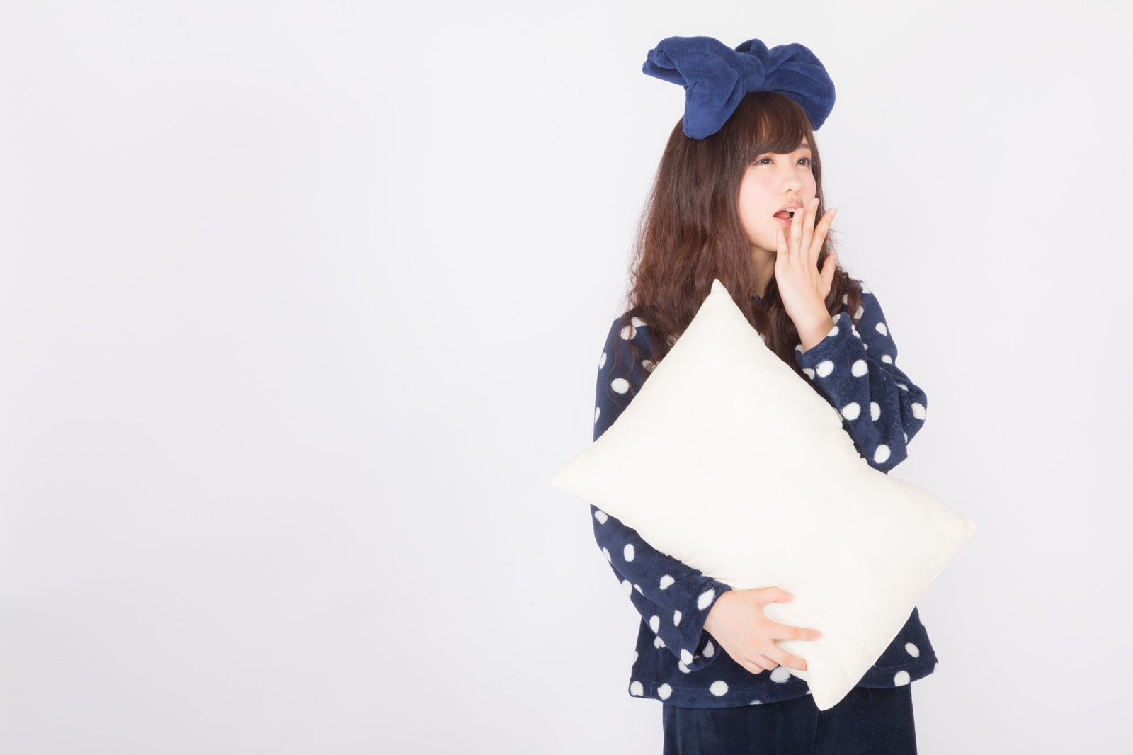 パジャマに枕を持ってあくびをしている女性