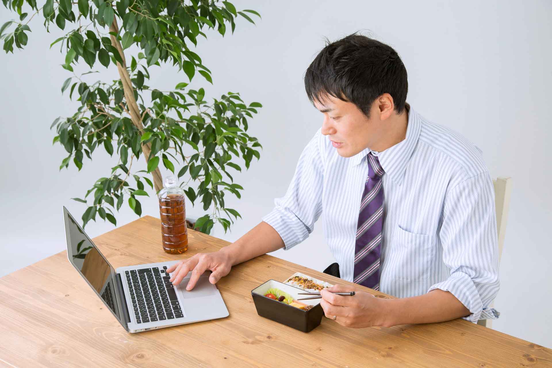デスクで仕事をしながらお弁当を食べているサラリーマン
