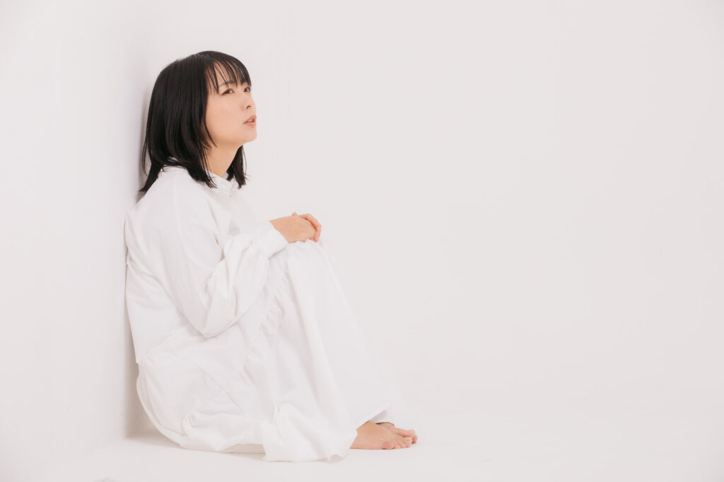 壁を背にしてパジャマ姿で天井を眺めている女性