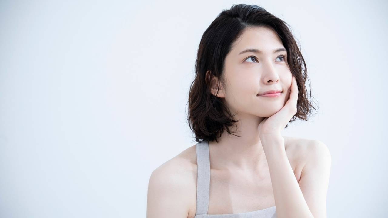 白い部屋で顎に手をあてて悩んでいる様子の女性