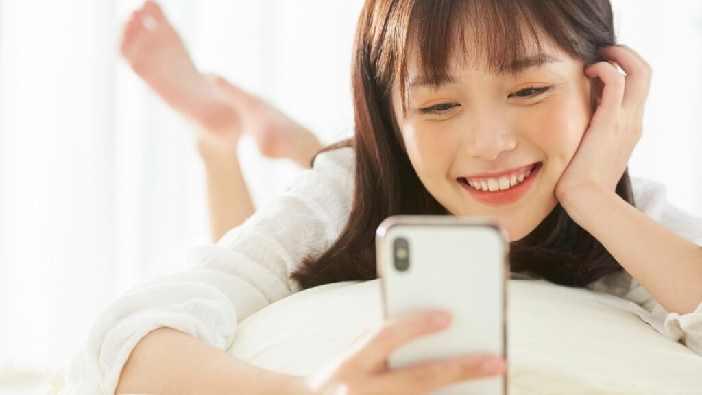 ベッドに寝転び笑顔でスマホを見ている女性