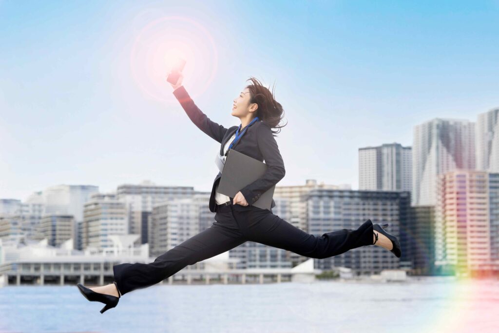 スマホを持ってジャンプしているスーツ姿の女性
