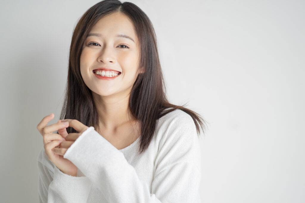 グレー背景の前で笑顔でほほ笑んでいるロングヘアの女性