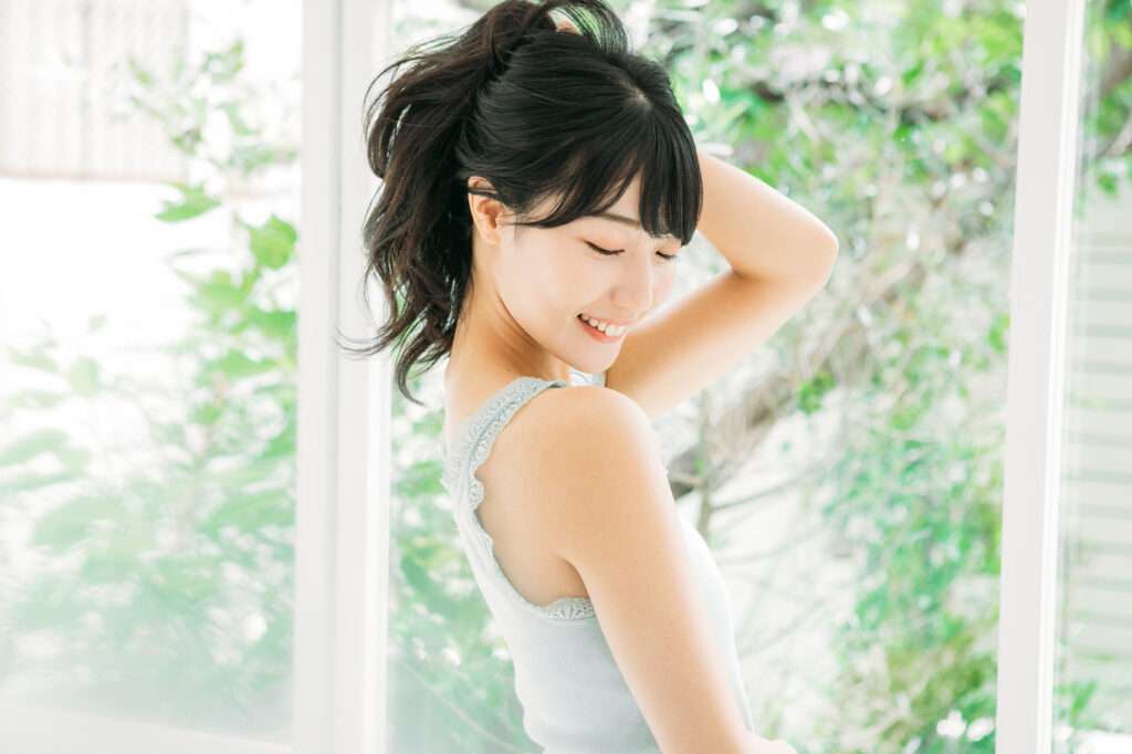 後ろ髪をかき上げてまとめている笑顔のタンクトップ女性
