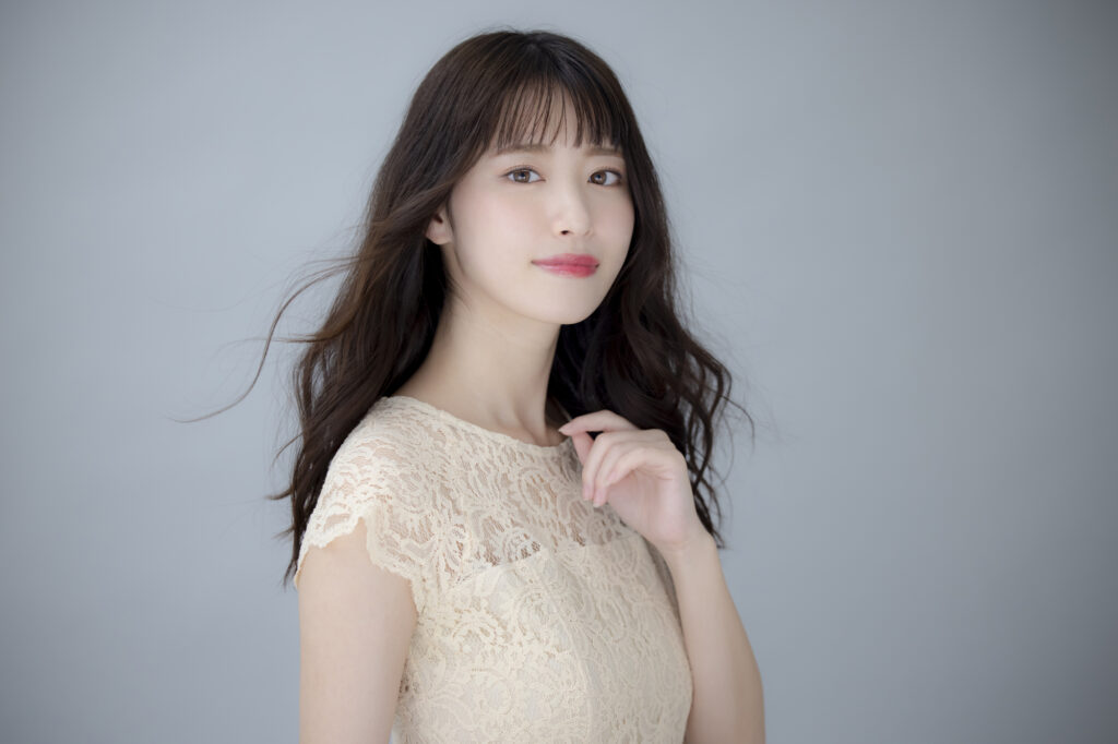 グレー背景の前でポーズをとっている白いワンピース姿の女性