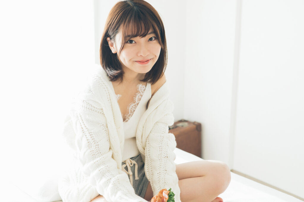 ベッドに座って微笑んでいる20代初めぐらいの女性