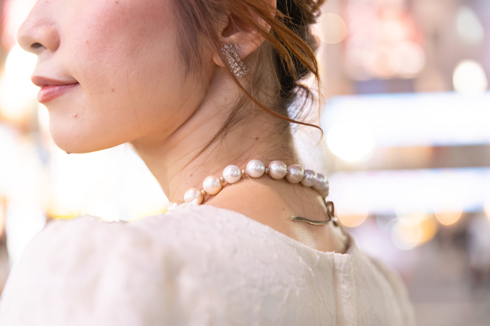 夜の街を背景にこちらを振り向く白いドレス姿の女性の首元
